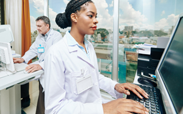 woman of color in a lab coat looking at computer